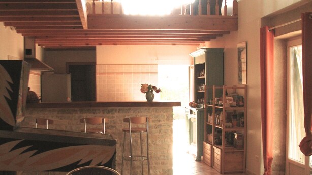 Un coin repas avec une table ronde et des chaises, une cuisine à l’arrière-plan et un escalier menant à un niveau supérieur.