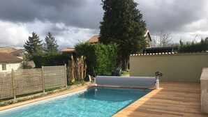 A rectangular swimming pool with clear blue water, surrounded by a wooden deck.