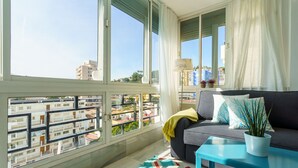 Un salon moderne avec un canapé gris, une table basse bleue et une vue sur le paysage urbain, visible à travers de grandes fenêtres.