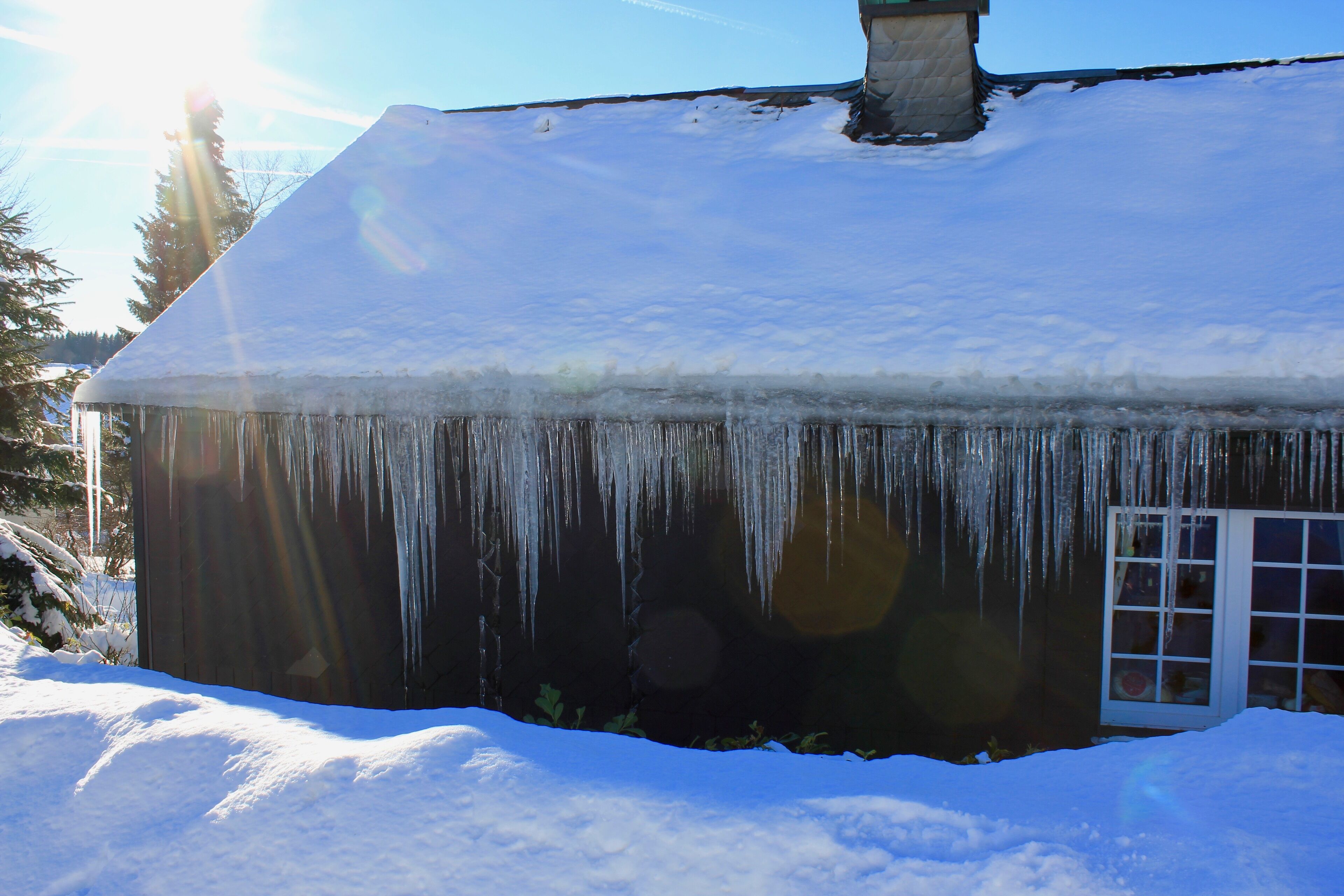 Una casa con tejado cubierto de nieve y estalactitas colgando de los aleros.