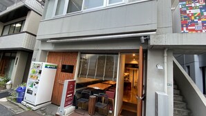 A modern two-story building with a dining area visible through the glass door. - New Minka Guest House (Tokyo)