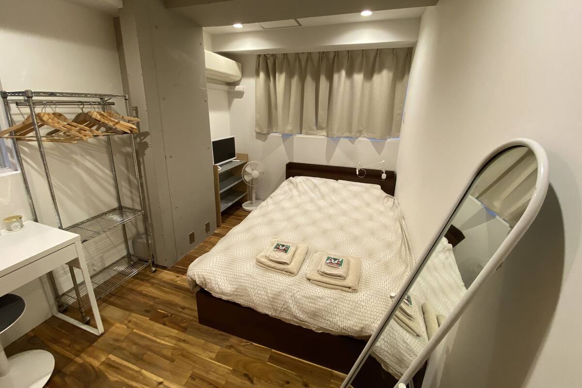 Habitación de hotel compacta con cama, escritorio, espejo, armario y un pequeño espacio para sentarse.