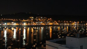 Vista nocturna de un puerto con barcos y un paisaje urbano al fondo.