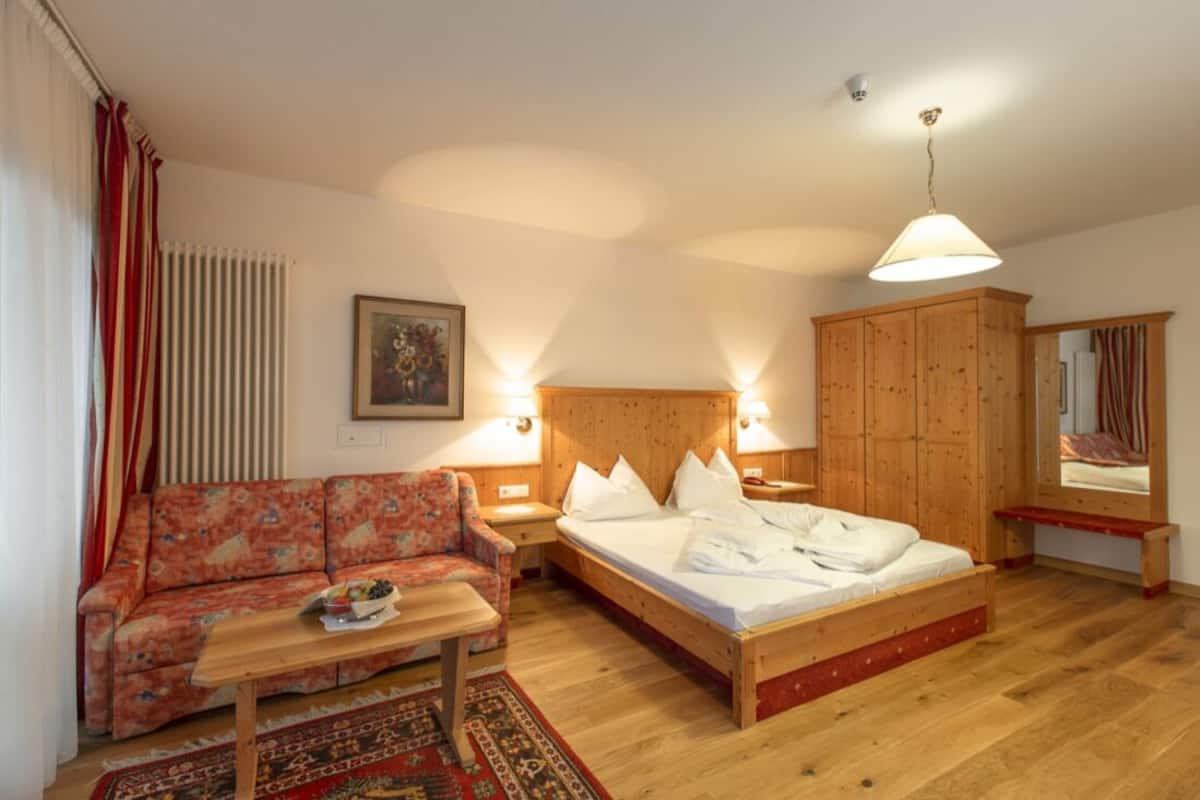 Un dormitorio con cama de madera, un sofá, una mesita y un armario.