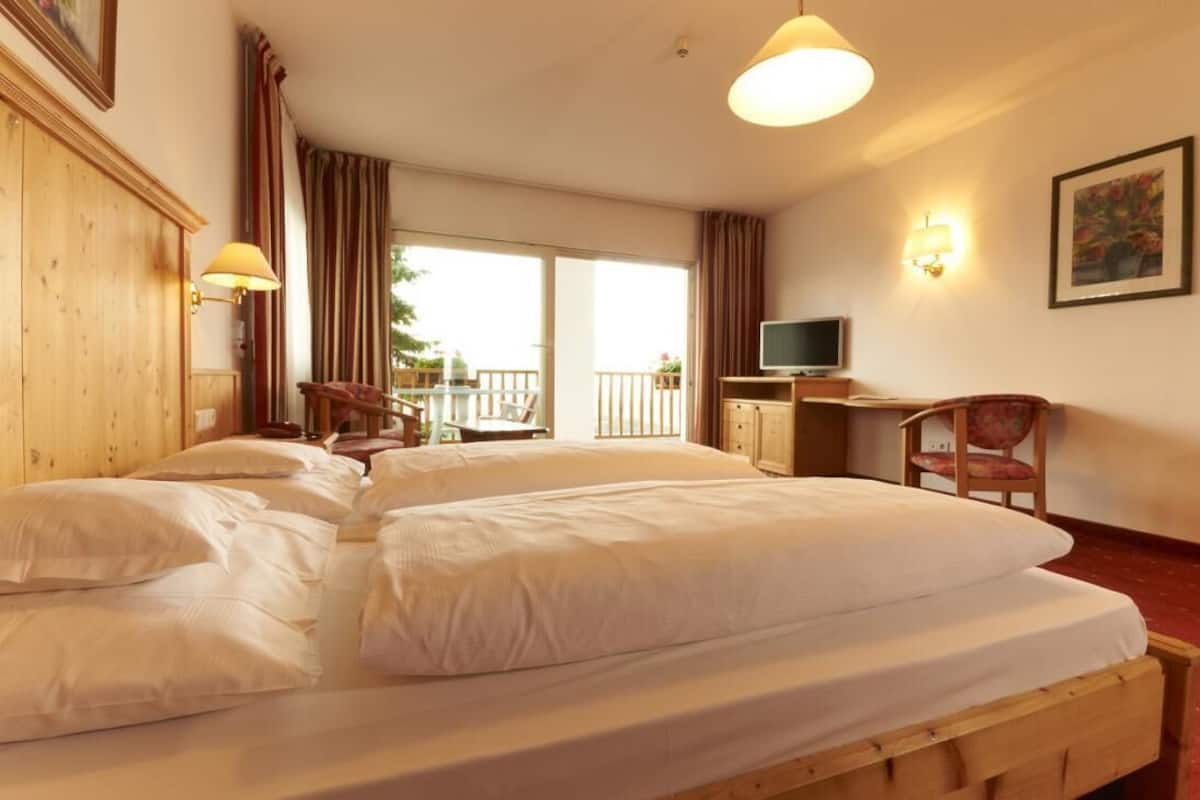 Habitación de hotel con dos camas, un escritorio con televisor y un balcón con vistas.