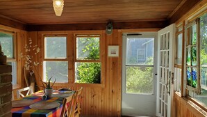 En mysig matplats med träväggar, ett bord dukat med en färgglad duk, stolar och en bänk.