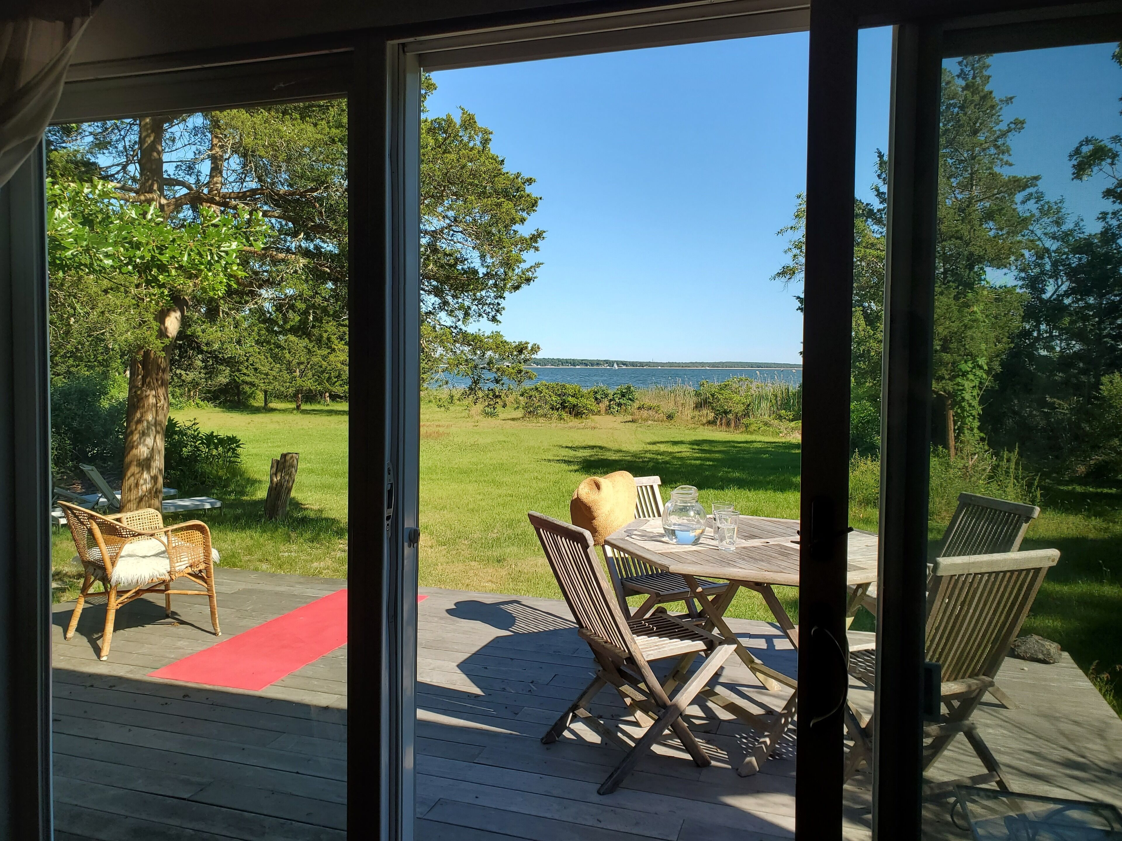 Een terras met buitenmeubilair, een glazen deur en uitzicht op een meer en bomen.