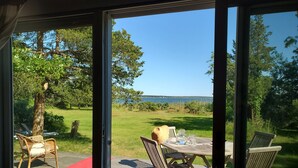En terrass med utemöbler och en glasdörr som leder ut till en vacker utsikt över en sjö och träd.
