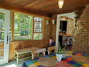 Ein gemütliches Zimmer mit Holzwänden, einer Bank, einem Tisch mit bunten Tischdecken und Blick auf den Garten durch große Fenster.