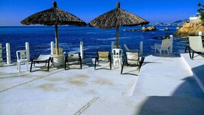 Eine Strandlounge mit Reetdachschirmen und weißen Liegestühlen.