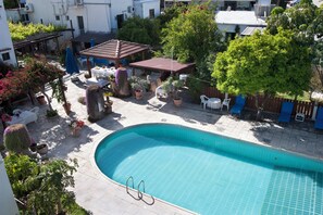 A swimming pool with a tiled deck, surrounded by potted plants and outdoor furniture.