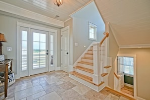 A spacious foyer with a staircase leading to an upper level, large glass doors, and a view of the outdoors.