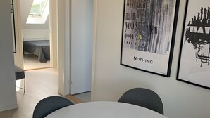 A modern dining area with a round table and four chairs, a skylight above a bed, and two framed artworks on the wall. - Just Sleep (Brande)