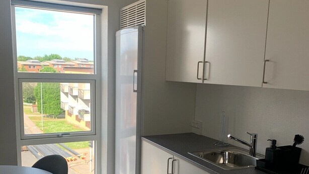 A modern kitchen with white cabinets, a stainless steel sink, and a window overlooking a residential area. - Just Sleep (Brande)