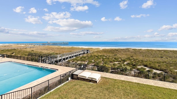 A swimming pool with a deck, a beach view, and a pier in the background. - Oceanfront Beach Condo with Private Balcony, Short Walk to Pool and Beach by RedAwning (Fernandina Beach)