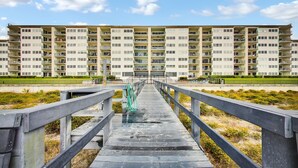 A long wooden bridge leading to a high-rise residential building with multiple balconies. - Oceanfront Beach Condo with Private Balcony, Short Walk to Pool and Beach by RedAwning (Fernandina Beach)