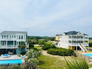Two-story buildings with balconies and a pool overlook well-manicured lawns and a sandy beach area.