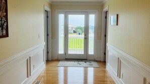 A hallway with a wooden floor, white walls, and a glass door leading to a balcony. - Salt, Sand And Sudds 5 Bedroom Home by RedAwning (Supply)