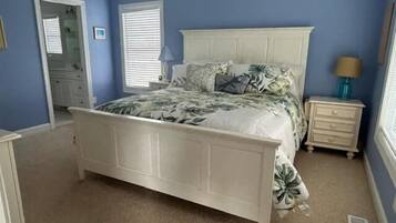 A bedroom with a white bed, a nightstand, a lamp, and a window with blinds.