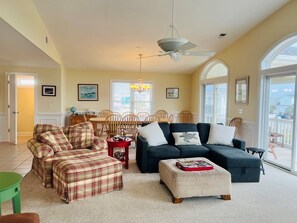 A spacious living room with a dining area, a ceiling fan, and large windows. - Salt, Sand And Sudds 5 Bedroom Home by RedAwning (Supply)