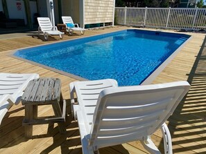 A swimming pool with white lounge chairs and a wooden deck. - Salt, Sand And Sudds 5 Bedroom Home by RedAwning (Supply)
