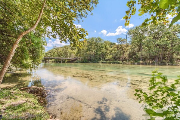 Un río con agua cristalina, rodeado de  árboles y un puente al fondo.
