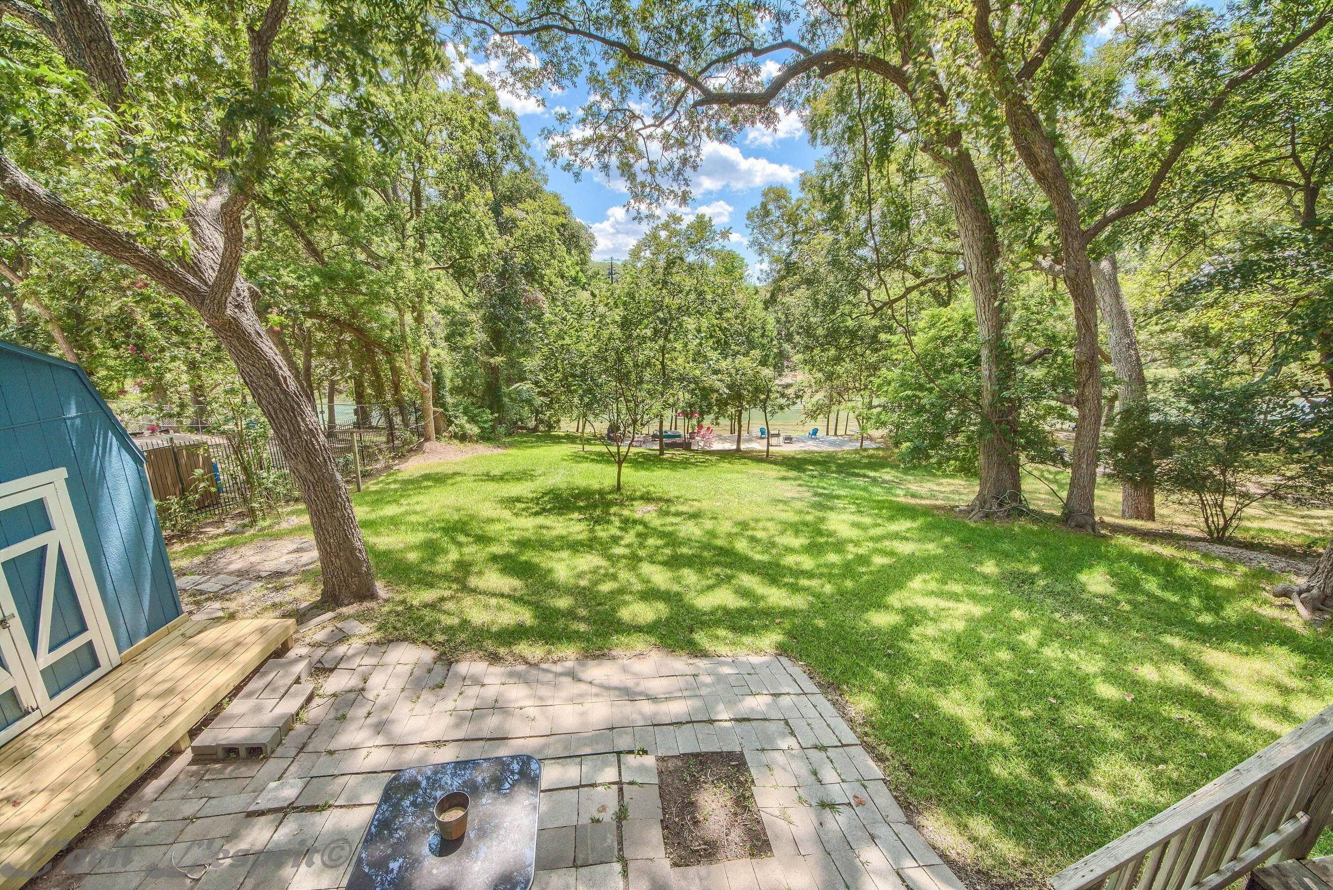 A backyard with a wooden deck, a hot tub, and a blue shed.