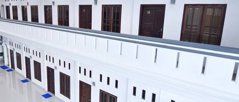A long corridor with multiple doors, each marked with a number, and a balcony railing.
