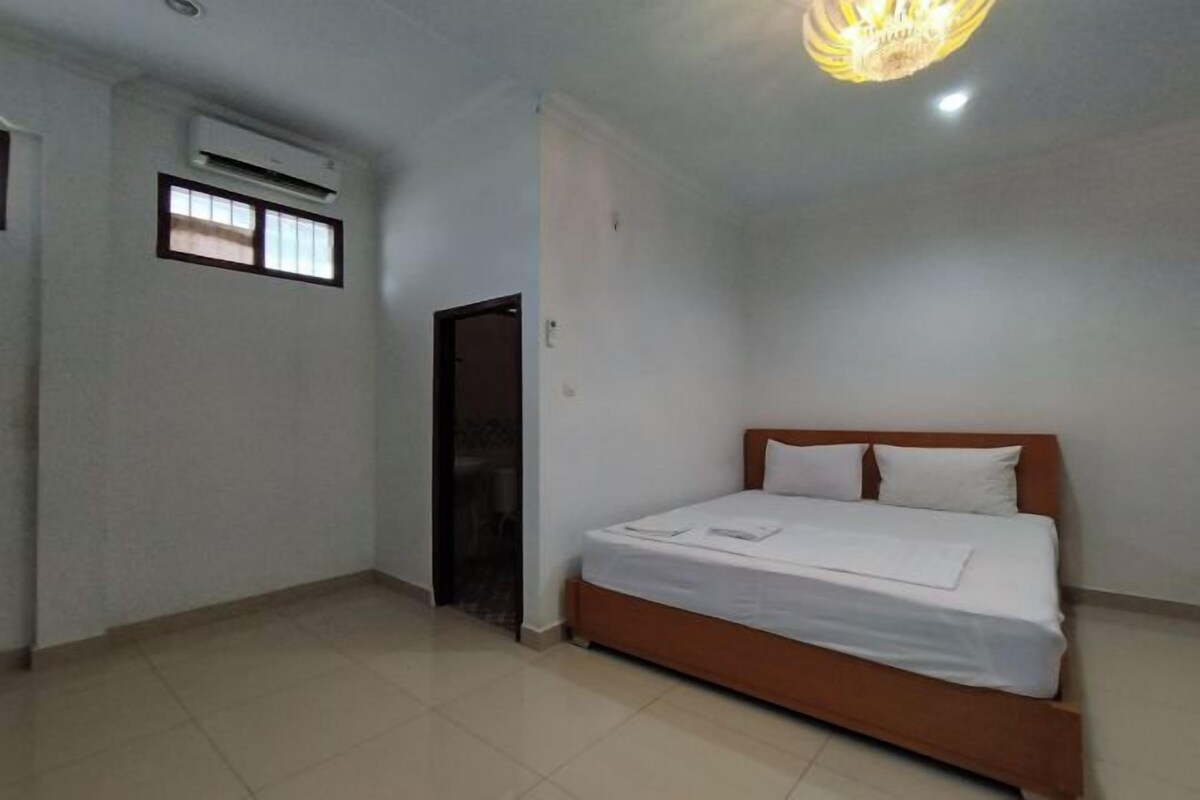 A bedroom with a bed, a window, an air conditioning unit, and a door.