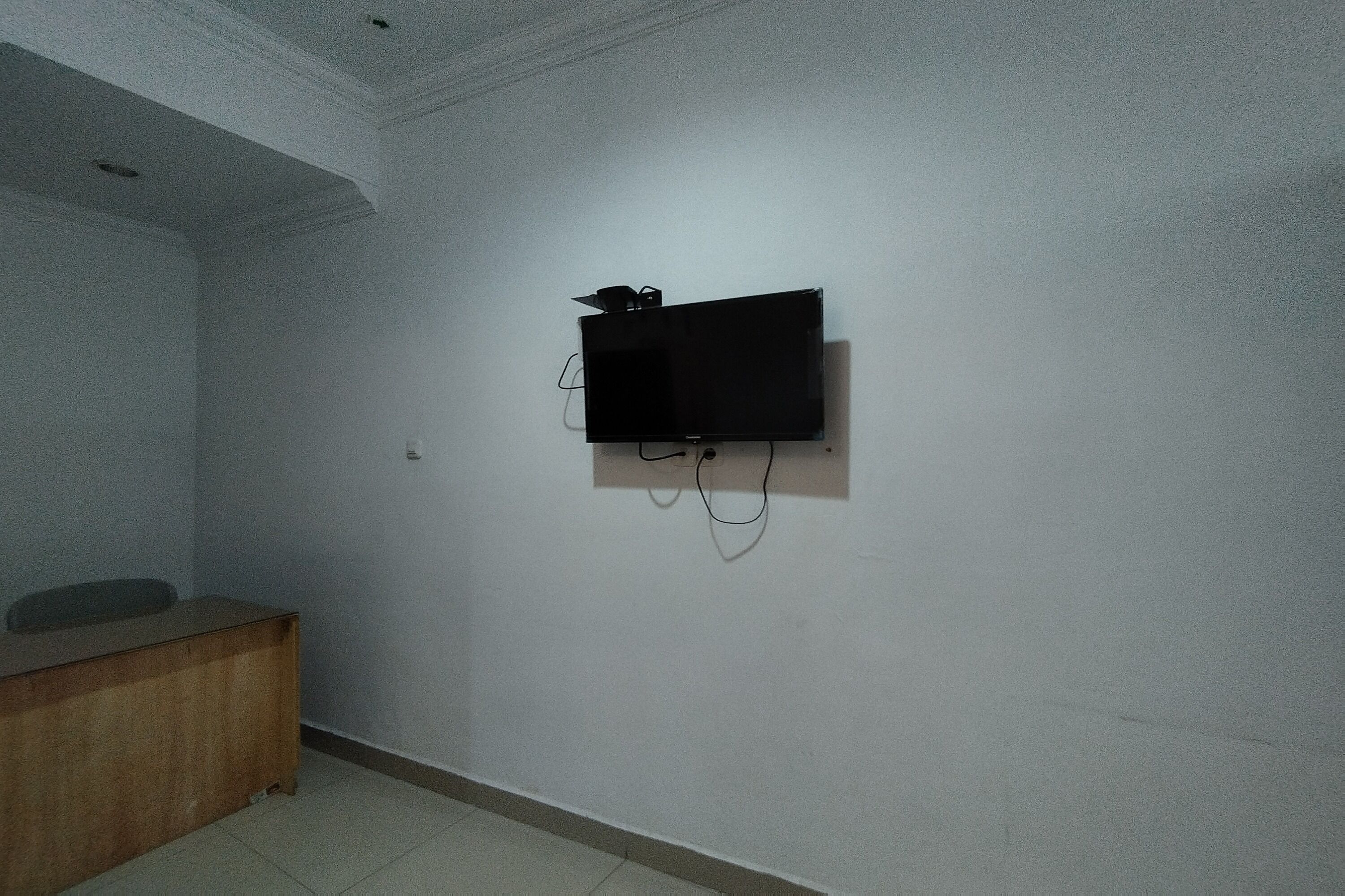 Une chambre dotée d’un téléviseur à écran plat fixé au mur, d’un bureau en bois et d’un sol carrelé.