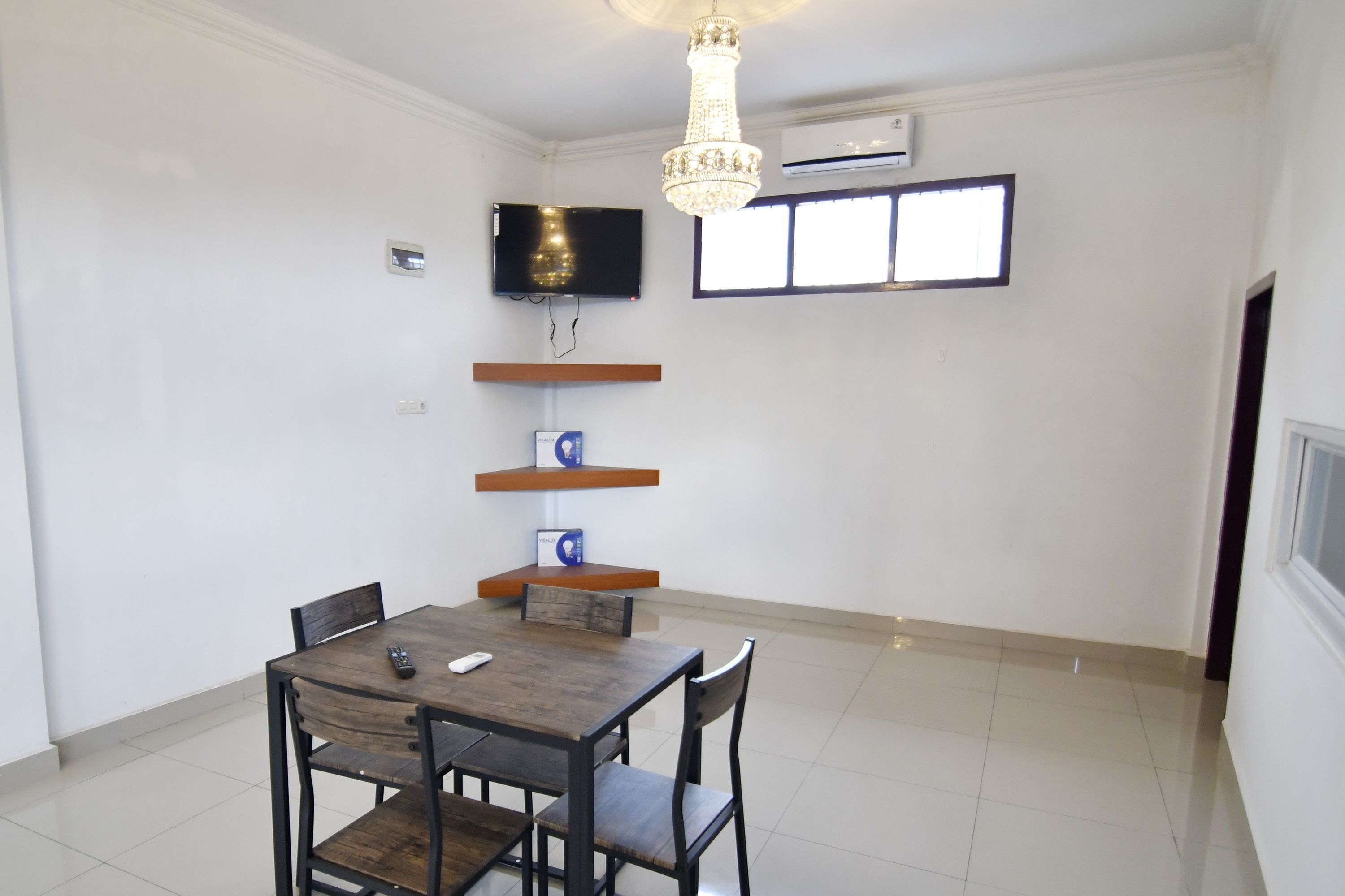 A dining area with a table and chairs, a chandelier, a mounted TV, and a window with blinds.