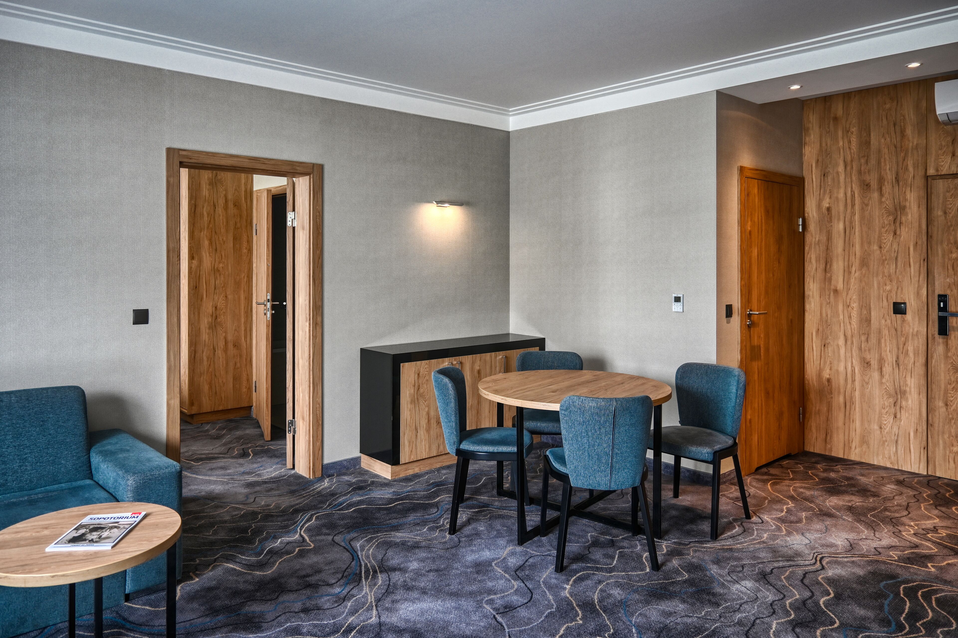 Una habitación de hotel con un sofá azul, una mesa redonda de madera y un comedor con cuatro sillas.