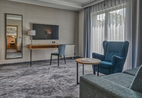 Una habitación de hotel con una cama grande, un escritorio con silla, televisión y ventana con cortinas.