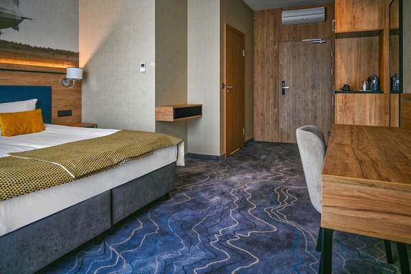 Une chambre d’hôtel comprenant un lit, une table de chevet, une lampe, une armoire et un bureau avec une chaise.