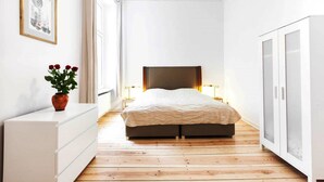 A bedroom with a bed, bedside lamps, a dresser, a potted plant, and a wardrobe. - Brücken Deluxe 1 - 3 (Berlin)