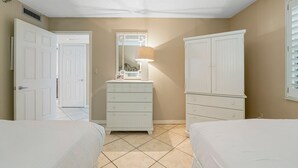 Une chambre avec deux lits, une commode, un miroir et une lampe.