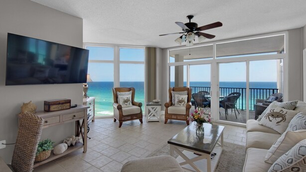 A spacious living room with a large TV, comfortable seating, a ceiling fan, and a balcony with ocean views. - Jade East 1220 (Destin)