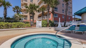 A swimming pool with a hot tub, surrounded by lounge chairs and palm trees. - Jade East 1220 (Destin)