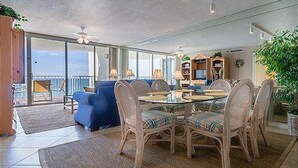 A spacious living area with a glass door leading to a balcony, wicker furniture, and a television. - Gulfside 0702 at Hidden Dunes - 1149893 (Miramar Beach)