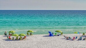 A beach with white sand and turquoise water. There are several green umbrellas and beach chairs. - Gulfside 0702 at Hidden Dunes - 1149893 (Miramar Beach)