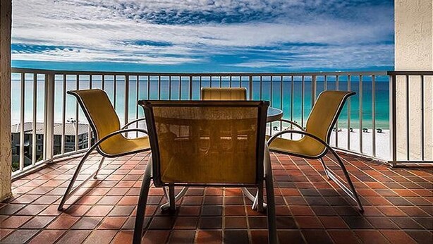 A balcony with a view of the beach, featuring a table and two chairs. - Gulfside 0702 at Hidden Dunes - 1149893 (Miramar Beach)