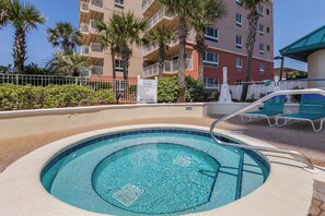 Una piscina con un jacuzzi, rodeada de sillas de descanso y palmeras.