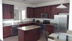 A modern kitchen with dark wood cabinets, granite countertops, stainless steel appliances, and a central island.