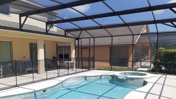A swimming pool with a sunshade structure, a patio area with seating, and a view of a building in the background.