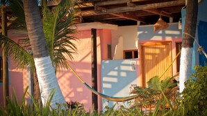 A hammock between palm trees, a wooden ceiling, and a pink and blue building with a door. - Small Luxury Hotel, Hideaway Near Acapulco on the Beach (Coyuca de Benitez)