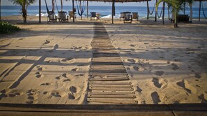 A beach with a wooden walkway leading to a thatched structure with chairs and tables. - Small Luxury Hotel, Hideaway Near Acapulco on the Beach (Coyuca de Benitez)