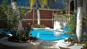 A swimming pool surrounded by palm trees and plants, with a brick wall and a building in the background. - Small Luxury Hotel, Hideaway Near Acapulco on the Beach (Coyuca de Benitez)