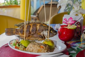 A plate with a grilled fish, lime halves, and rice.