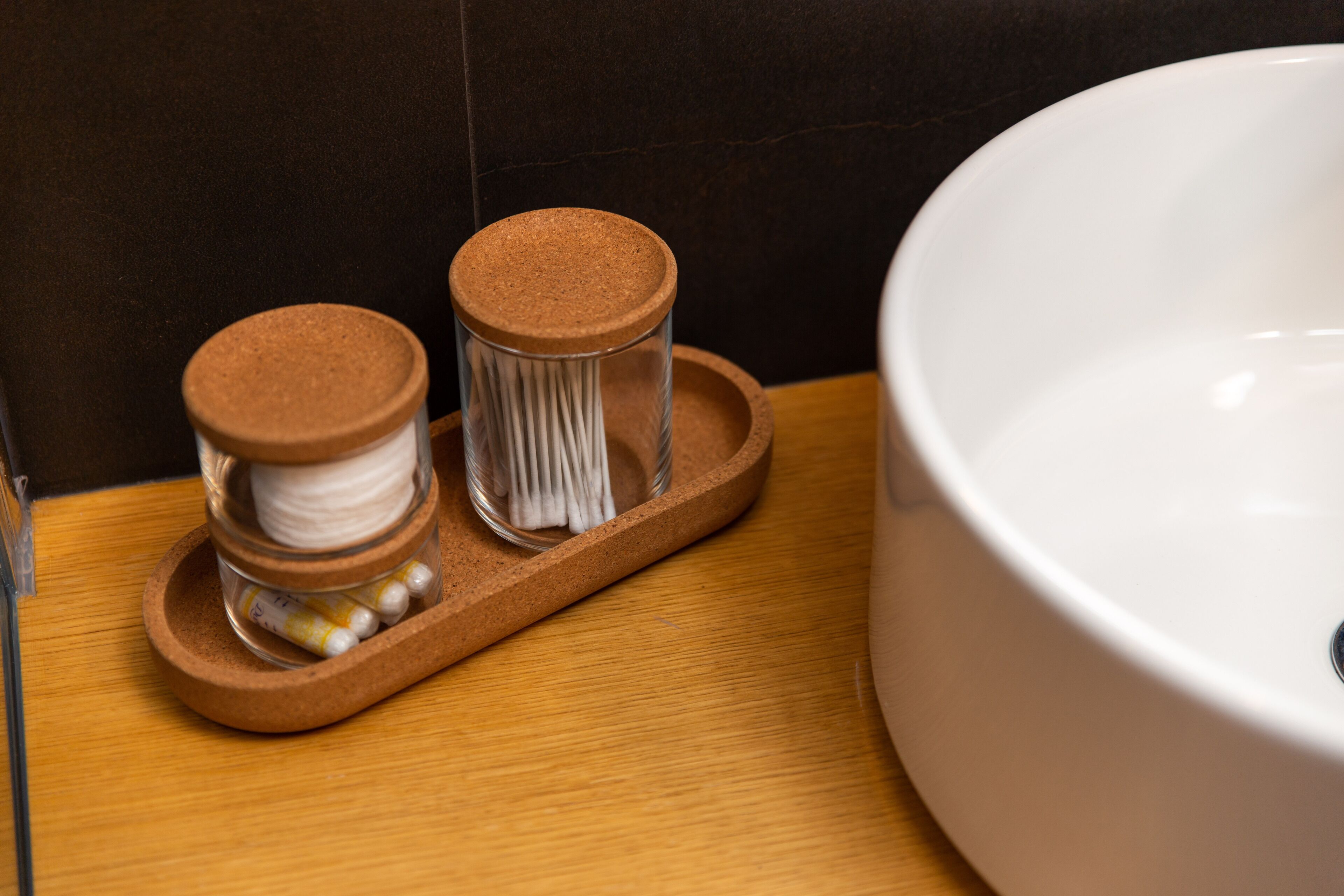 A bathroom with a wooden tray holding two glass jars with brown lids, one containing white cotton balls and the other containing cotton swabs.