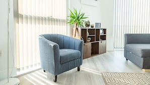 A modern living room with a blue armchair, a grey sofa, a wooden cabinet with decorative items, and a cityscape artwork on the wall.